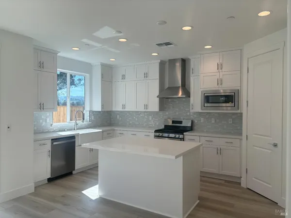 a kitchen with stainless steel appliances granite countertop a sink stove a refrigerator and white cabinets with wooden floor