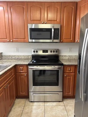 a kitchen with stainless steel appliances granite countertop a refrigerator a stove and a sink with wooden cabinets