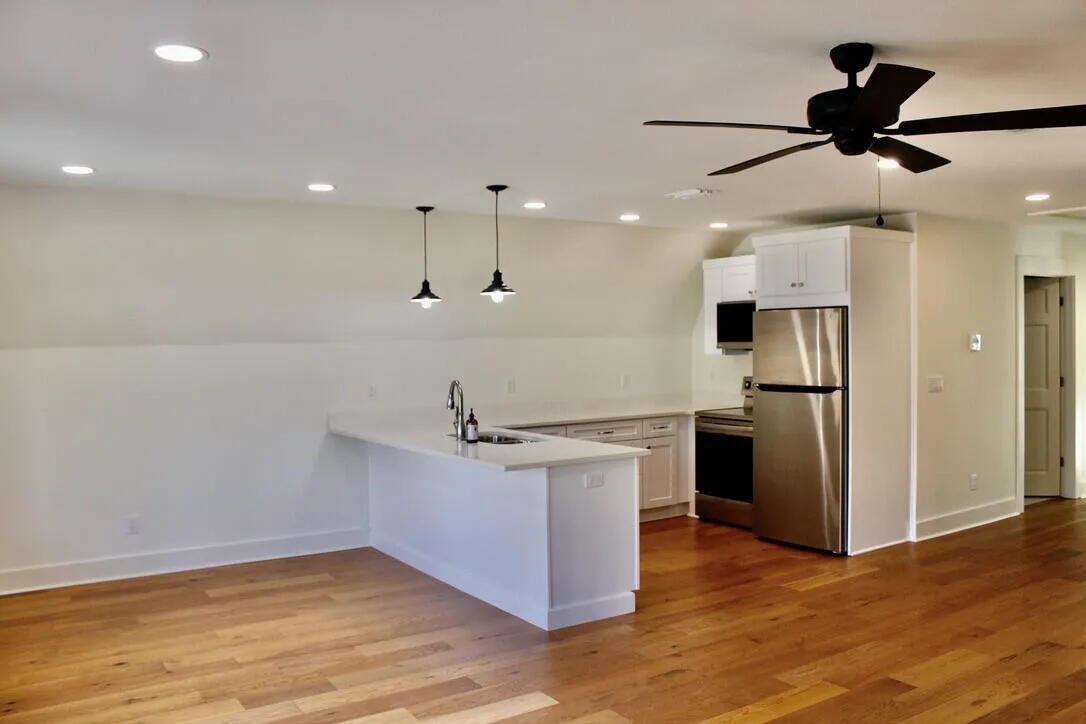 54 Davis Street DeFuniak Springs, FL 32435 - Photo 7 of 14 an empty room with wooden floor a ceiling fan and kitchen view