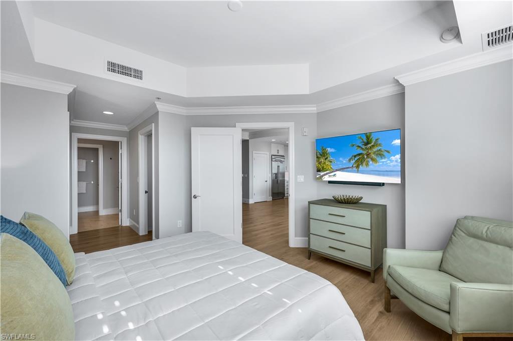 9115 Strada Place, Unit 5502 Naples, FL 34108 - Photo 19 of 48 Primary Bedroom featuring ornamental molding, light wood floors ,a tray ceiling and a wall mount TV.