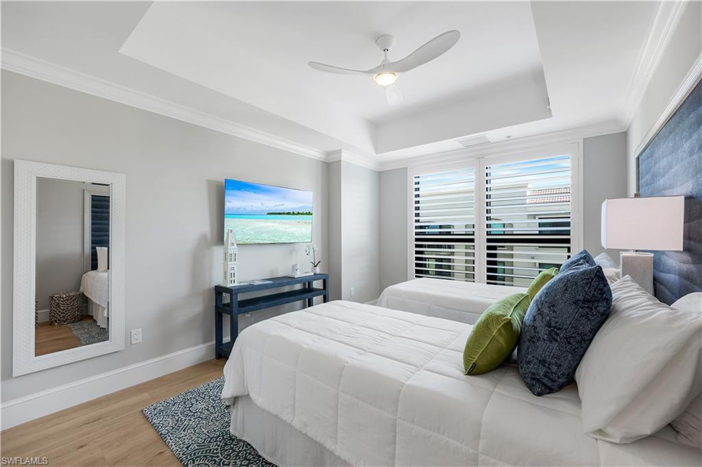 9115 Strada Place, Unit 5502 Naples, FL 34108 - Photo 27 of 48 Guest Bedroom featuring a tray ceiling, wood finished floors, ornamental molding, a ceiling fan and a wall TV