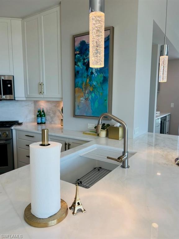 9115 Strada Place, Unit 5502 Naples, FL 34108 - Photo 7 of 48 Kitchen featuring decorative backsplash, white cabinetry, appliances with stainless steel finishes, light stone counters, and hanging light fixtures