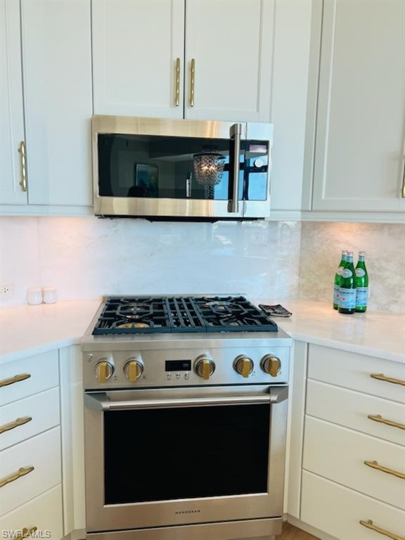 9115 Strada Place, Unit 5502 Naples, FL 34108 - Photo 9 of 48 Kitchen featuring stainless steel appliances, white cabinetry, light stone countertops, and backsplash