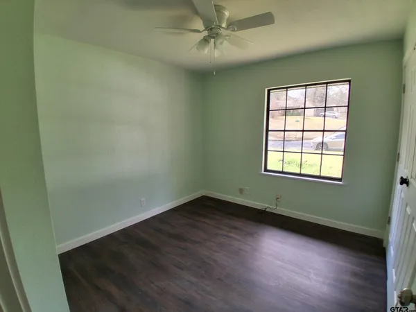 an empty room with wooden floor fan and windows