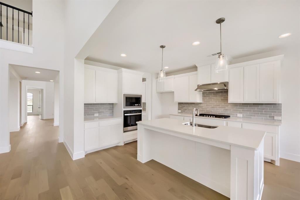 11465 Wulstone Road Fort Worth, TX 76052 - Photo 10 of 27 Bright kitchen featuring a central island with an undermount sink, white cabinetry, integrated stainless steel appliances, a subway tile backsplash, and recessed lighting