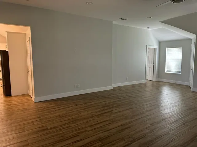 a view of an empty room with wooden floor and a window
