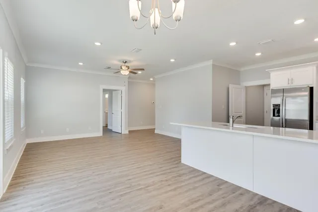 a view of an empty room and kitchen with wooden floor