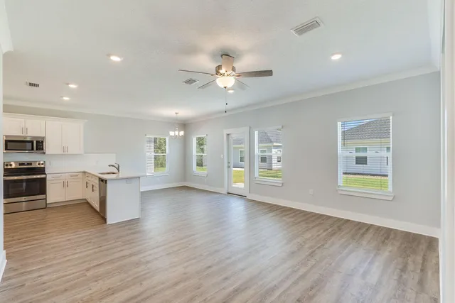 a view of an empty room with kitchen and window