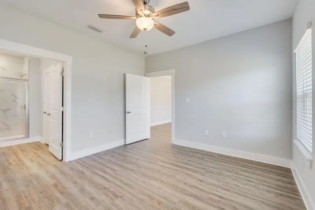 an empty room with wooden floor fan and windows