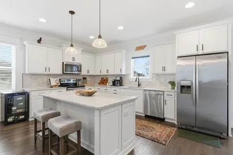 a kitchen with stainless steel appliances granite countertop a sink a stove a refrigerator and white cabinets