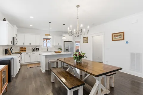 a open kitchen with stainless steel appliances kitchen island granite countertop a stove top oven a sink a dining table and chairs with wooden floor