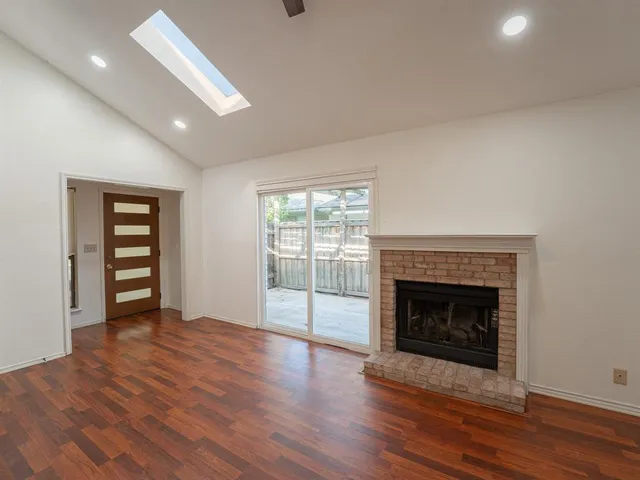 an empty room with wooden floor fireplace and windows