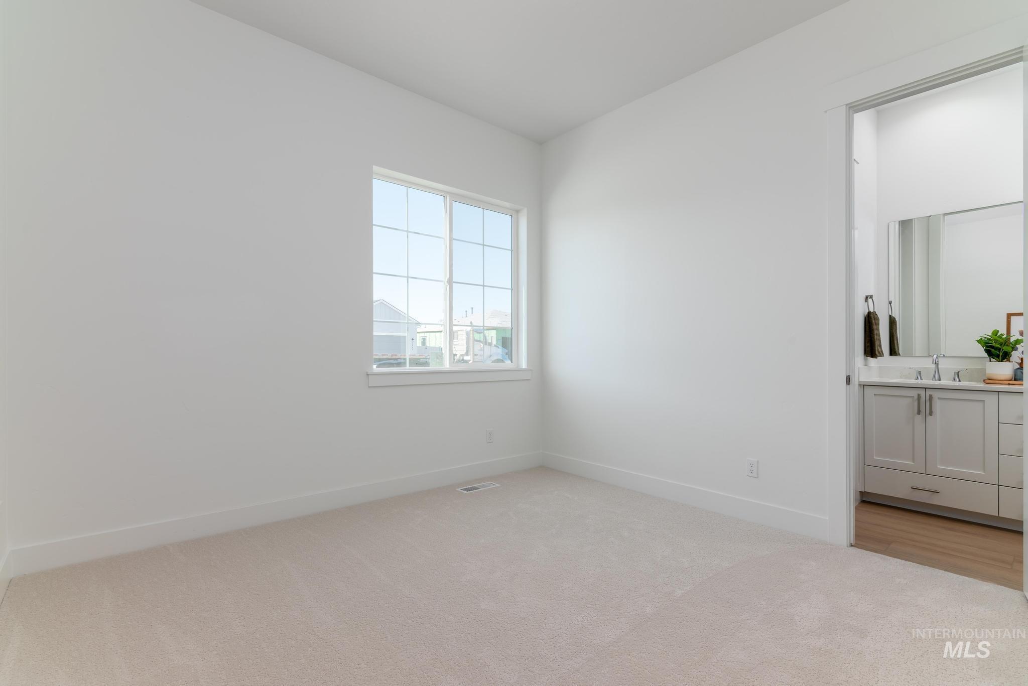 9074 West Moonglade Street Star, ID 83669 - Photo 23 of 40 Carpeted room featuring a multi-pane window and a doorway opening to a bathroom with a dual-sink vanity, mounted mirror, and wood-finish flooring