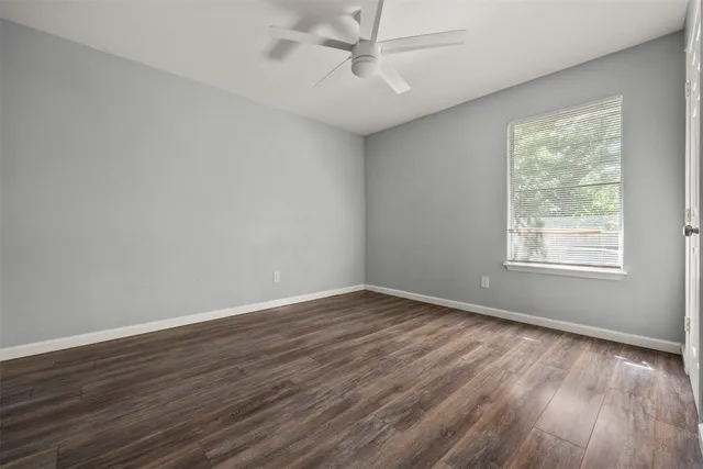 an empty room with wooden floor fan and windows