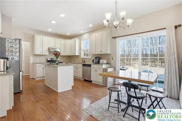 a kitchen with stainless steel appliances kitchen island granite countertop a refrigerator a stove a sink a dining table and chairs with wooden floor