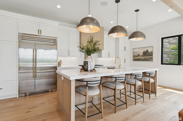 1400 Weber Wild Road Oakley, UT 84055 - Photo 12 of 55 Gourmet kitchen featuring a large central island with seating, a stainless steel built-in refrigerator, light wood-finish flooring, white cabinetry with gold-tone hardware, and three dome pendant lights