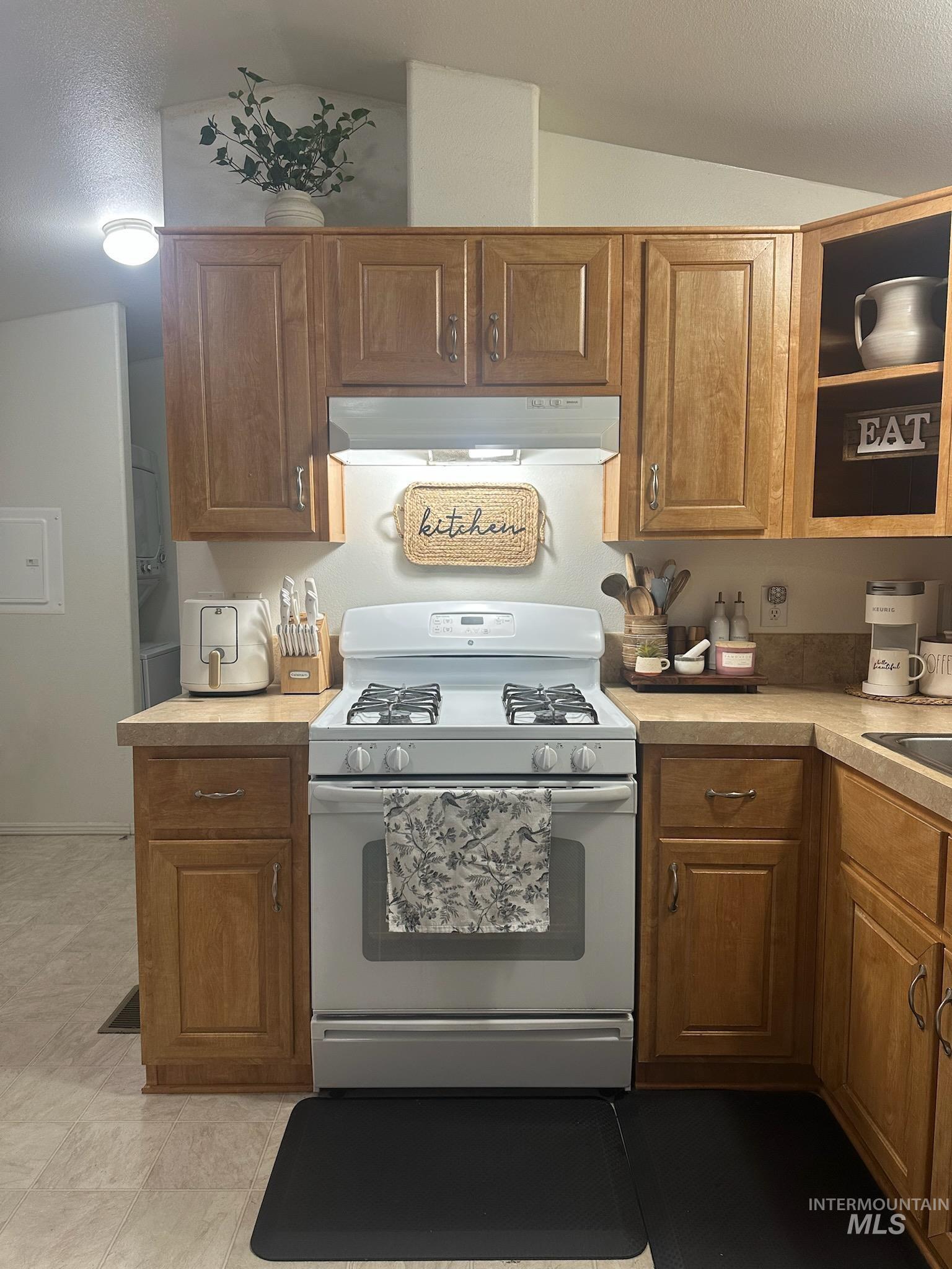 1171 North Sable Lane Boise, ID 83704 - Photo 12 of 19 Kitchen featuring white gas range oven, under cabinet range hood, light countertops, a textured ceiling, and brown cabinetry