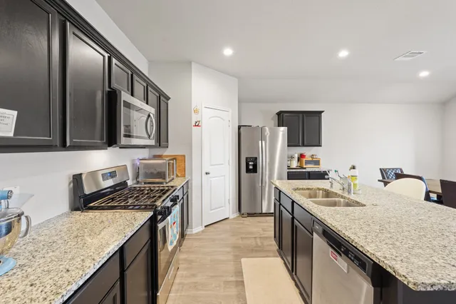 a kitchen with stainless steel appliances kitchen island granite countertop a refrigerator a stove top oven a sink dishwasher and wooden cabinets with wooden floor