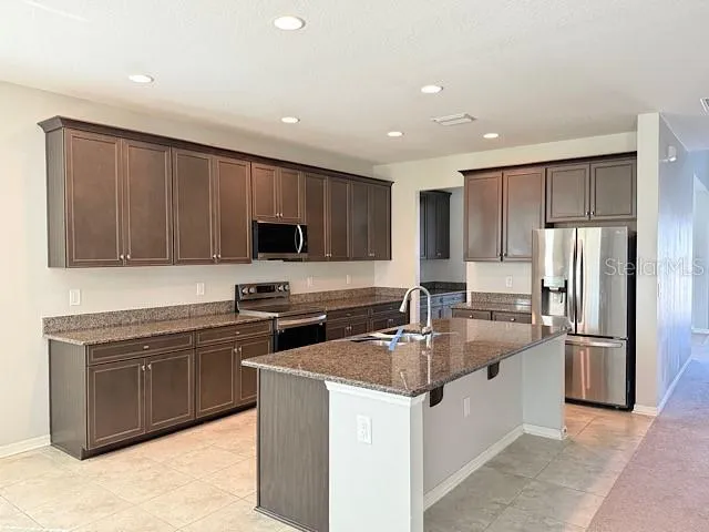 a kitchen with stainless steel appliances granite countertop a sink stove refrigerator and cabinets
