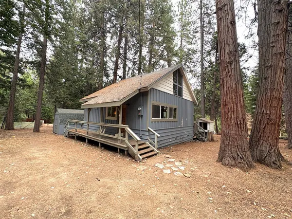a wooden house with large trees and wooden fence