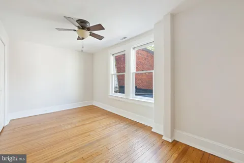 an empty room with wooden floor chandelier fan and windows