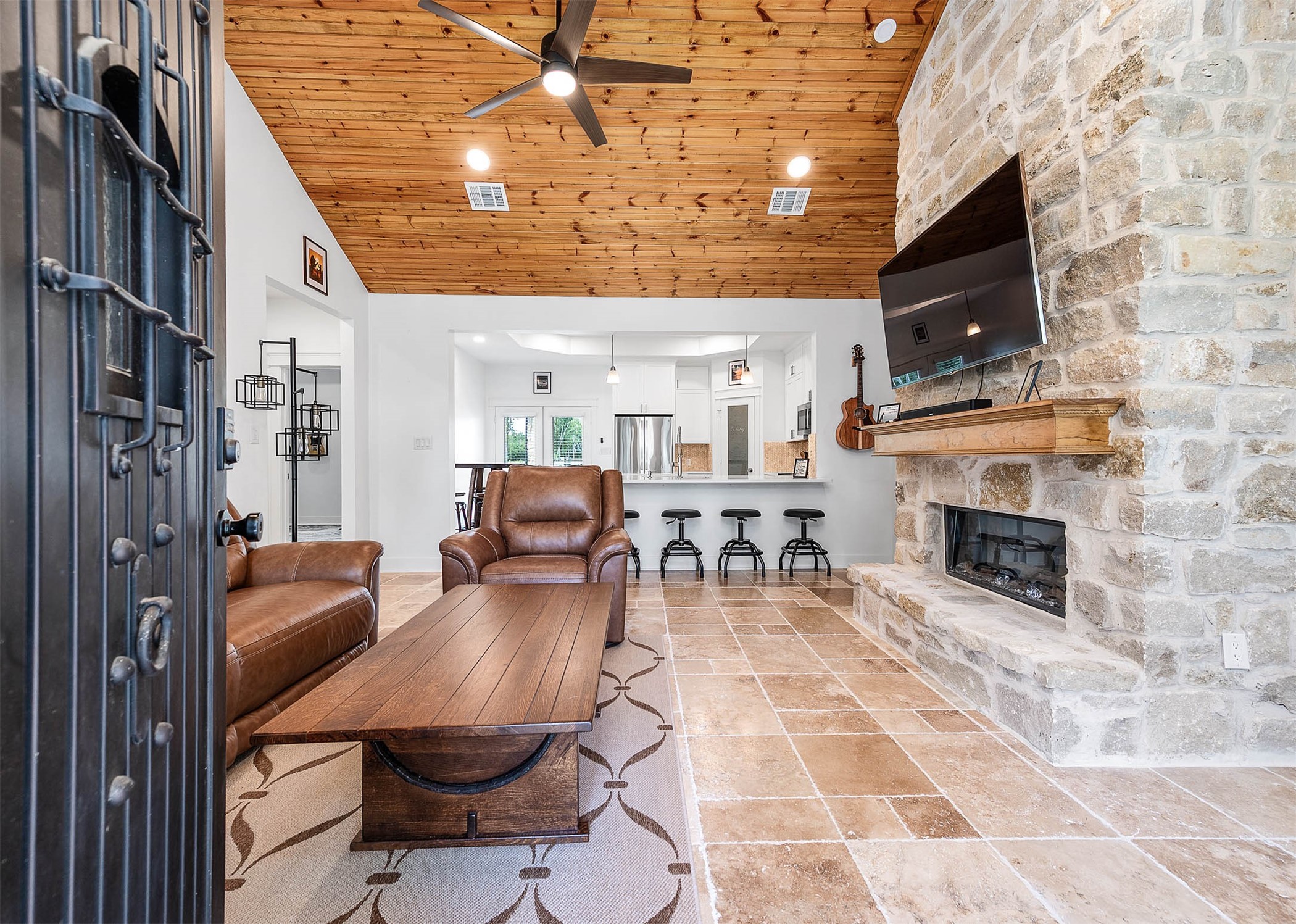 8032 Short Road Needville, TX 77461 - Photo 5 of 50 The spacious living area features soaring wood-accented ceilings, a striking stone fireplace, and an open-concept layout that flows seamlessly into the kitchen and dining area. Warm finishes and comfortable seating create the perfect space for relaxing or entertaining.