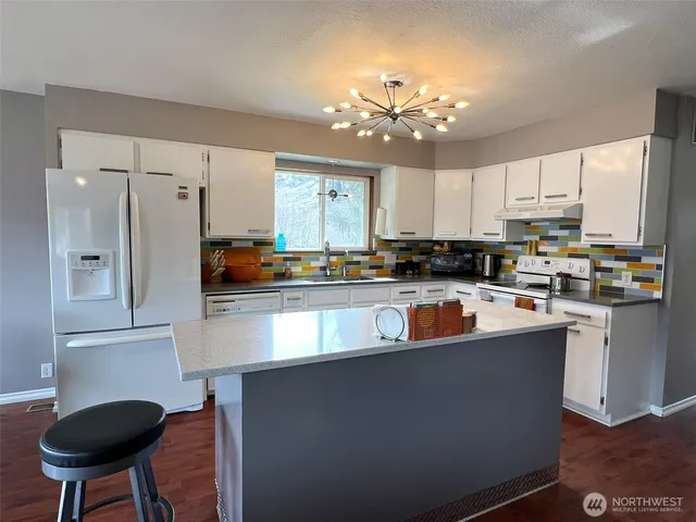 a kitchen with stainless steel appliances granite countertop a refrigerator a sink dishwasher a stove and a dining table with wooden floor