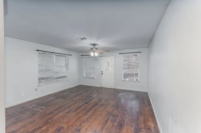an empty room with wooden floor cabinet and windows