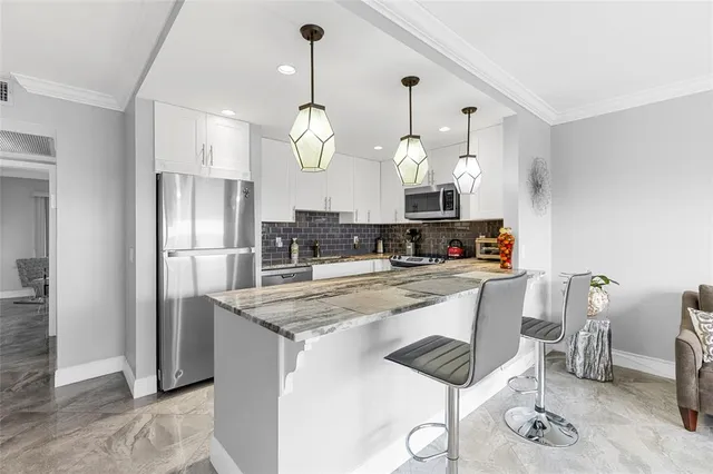 a kitchen with stainless steel appliances granite countertop a sink a stove a refrigerator and chairs