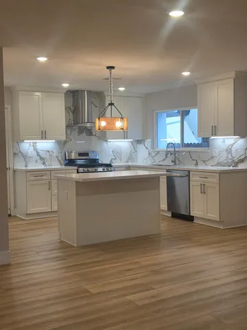 a kitchen with kitchen island a sink dishwasher a stove and white cabinets with wooden floor
