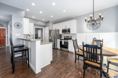 a kitchen with stainless steel appliances kitchen island granite countertop a dining table chairs and a refrigerator