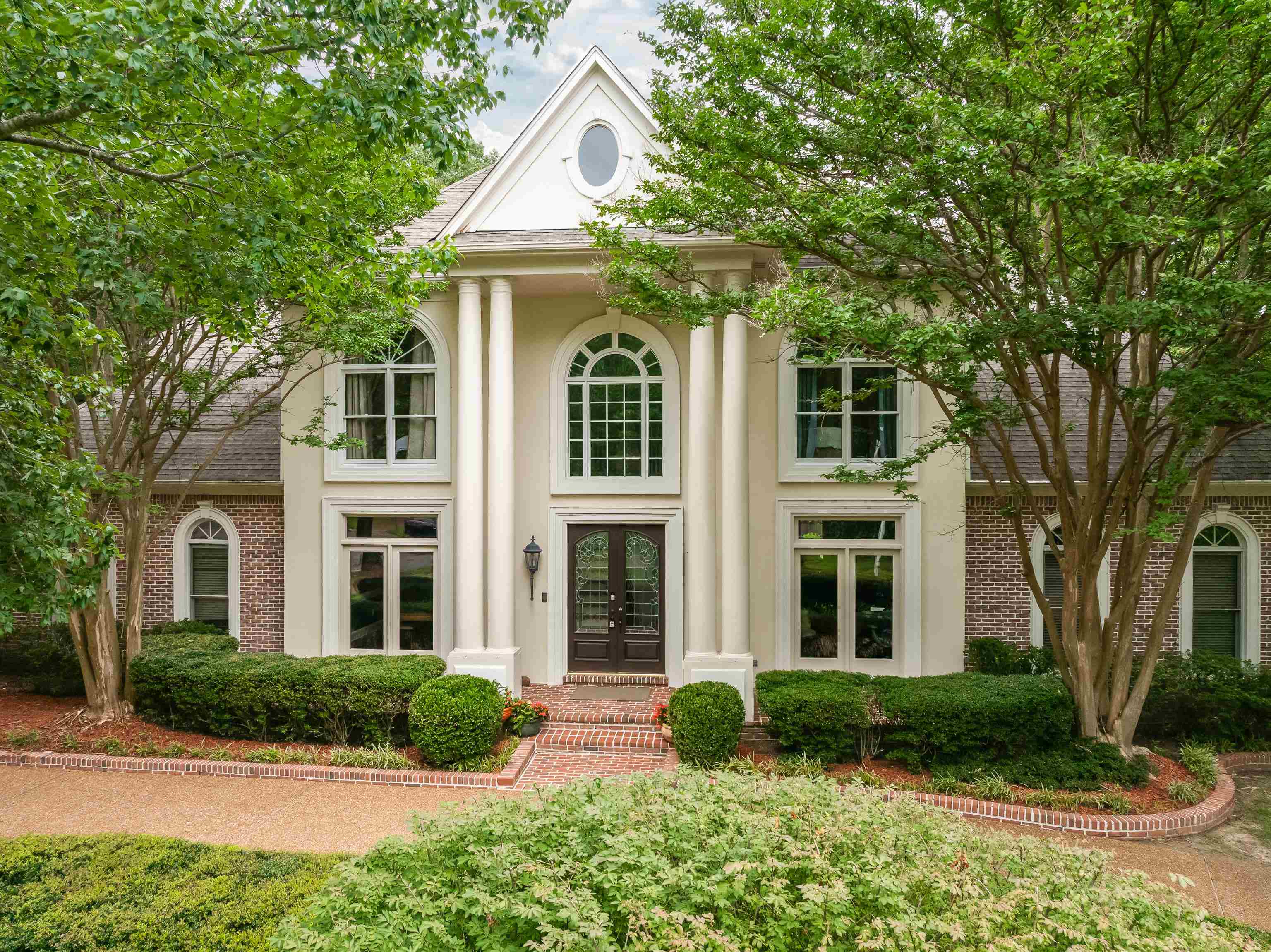 350 Bluff Ridge Cove Memphis, TN 38018 - Photo 3 of 37 Stately residence featuring a prominent portico with four columns, a double-door entry, a symmetrical facade with arched and rectangular windows, a brick accent wall, and a gabled roofline with an oval window