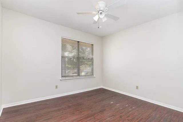 an empty room with wooden floor ceiling fan and window