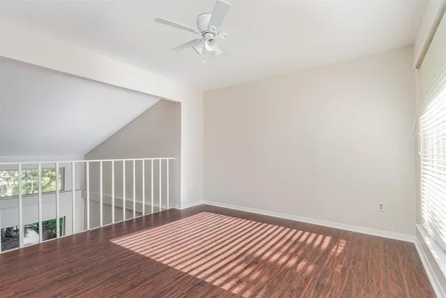 an empty room with wooden floor fan and windows