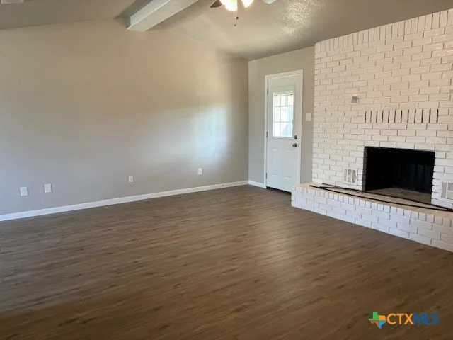 an empty room with wooden floor fireplace and windows