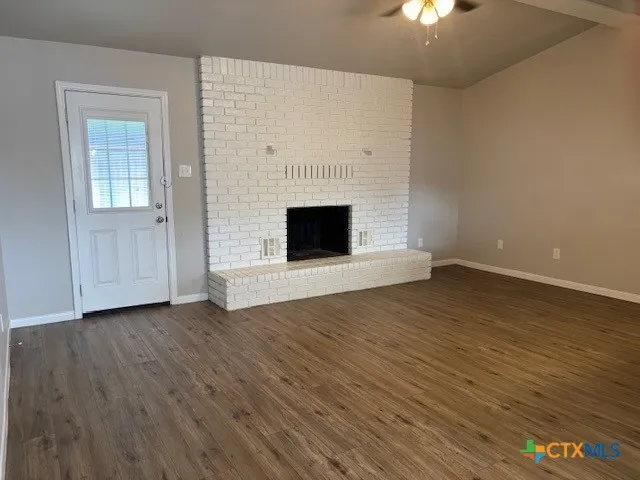 an empty room with wooden floor fireplace and windows