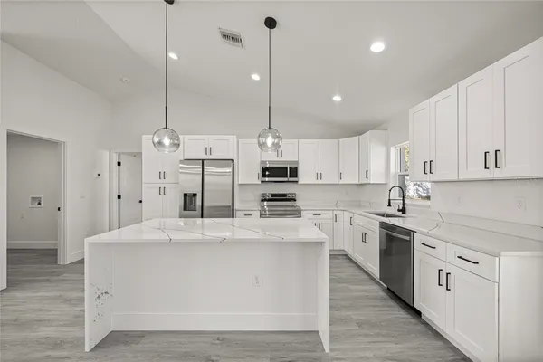 a large kitchen with stainless steel appliances kitchen island granite countertop a stove a sink a oven and white cabinets with wooden floor