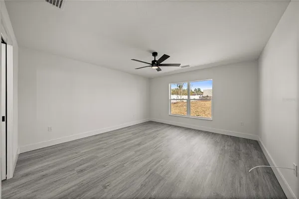an empty room with wooden floor chandelier fan and windows