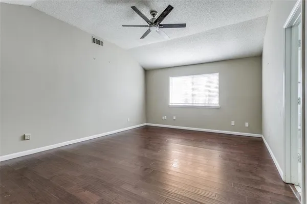 an empty room with wooden floor windows and fan