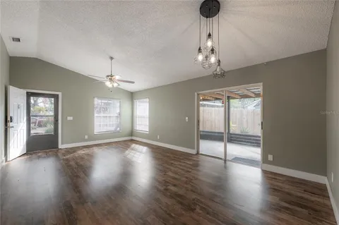 an empty room with wooden floor chandelier and windows