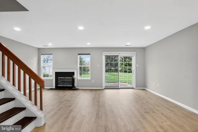 an empty room with wooden floor staircase and windows