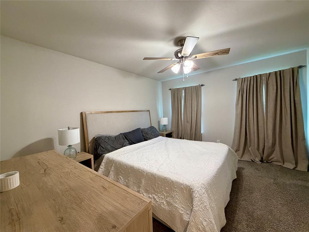 619 Mansfield Road Cleburne, TX 76031 - Photo 9 of 19 ceilings enhance this room, featuring a ceiling fan with integrated lighting, two windows with drapery, and neutral-toned carpeting