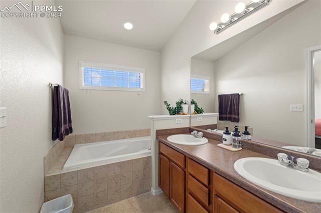 6310 Pilgrimage Road Colorado Springs, CO 80925 - Photo 25 of 31 Bathroom featuring tiled tub, tile patterned flooring, and vanity
