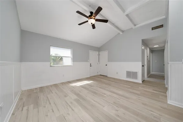 an empty room with wooden floor chandelier fan and windows