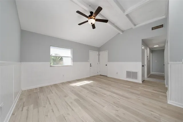 an empty room with wooden floor chandelier fan and windows