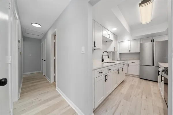 a large white kitchen with a refrigerator a sink dishwasher a stove and white cabinets with wooden floor