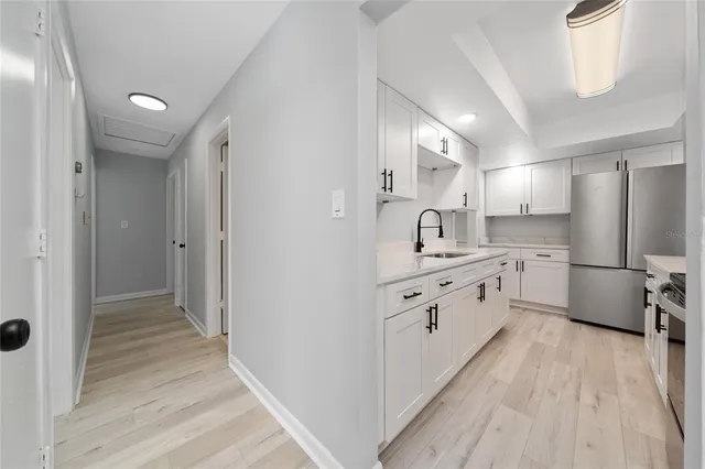 a large white kitchen with a refrigerator a sink dishwasher a stove and white cabinets with wooden floor