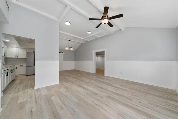 an empty room with wooden floor a ceiling fan and kitchen view