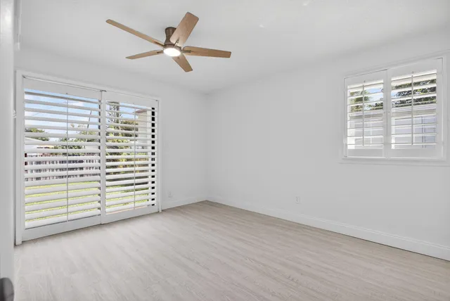 an empty room with wooden floor fan and windows