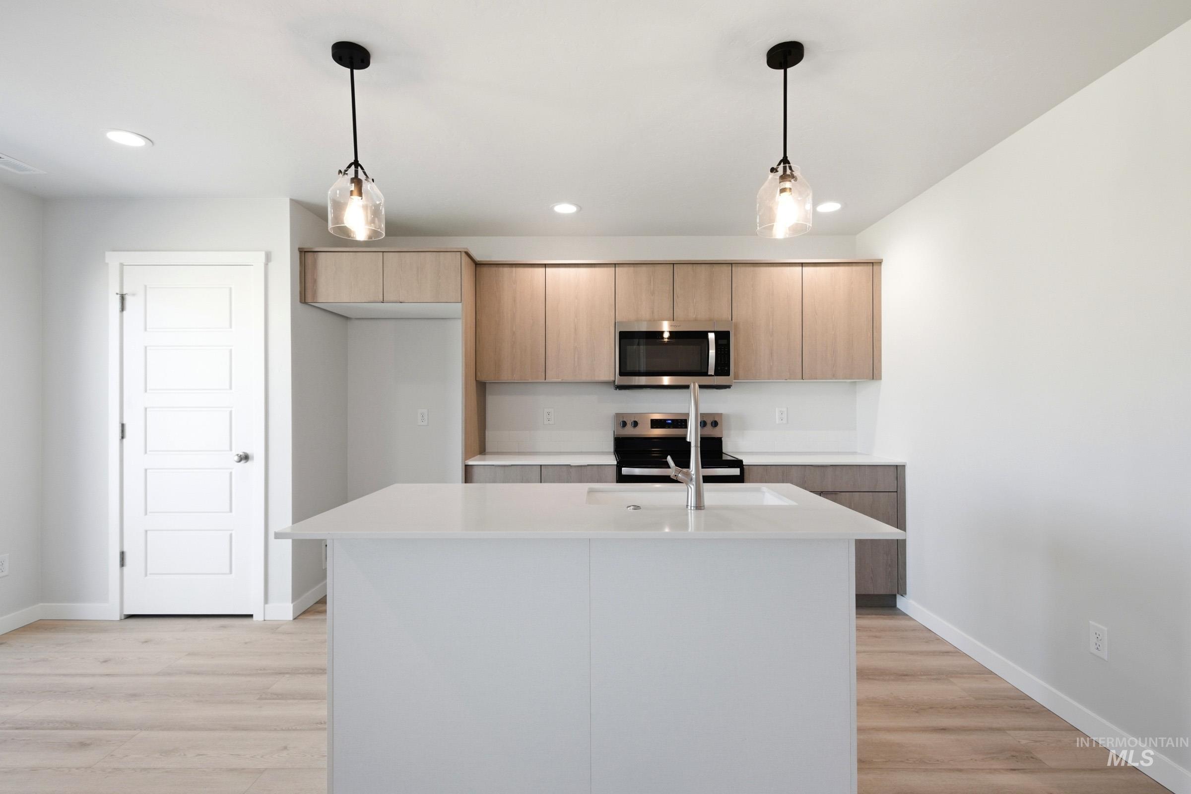 10812 Rutland Street Caldwell, ID 83605 - Photo 3 of 21 Modern kitchen featuring an expansive island with an undermount sink, pendant lighting, wood-finish flooring, light wood-finish cabinetry, and stainless steel appliances